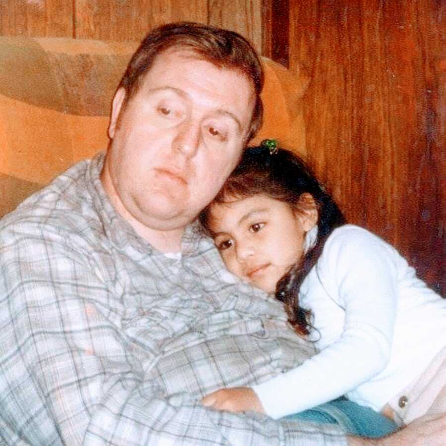 Young girl snuggles with her adoptive dad in the living room during some family quiet time