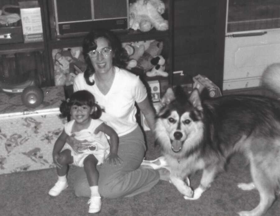Adoptive mom smiles while holding her adopted daughter on the floor next to their Alaskan Malamute