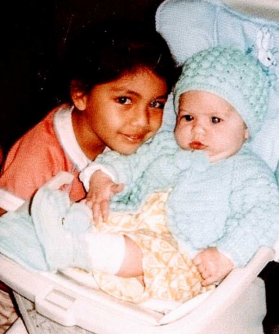 Young girl adopted from Mexico by parents in the U.S. smiles next to her newborn adopted sister