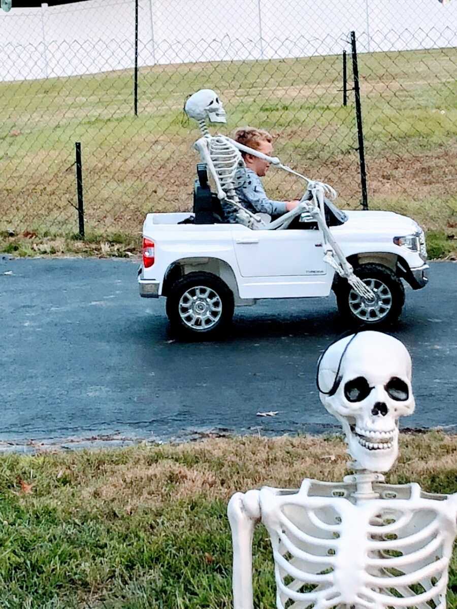 Little boy rides around in his toy truck with a Halloween skeleton decoration