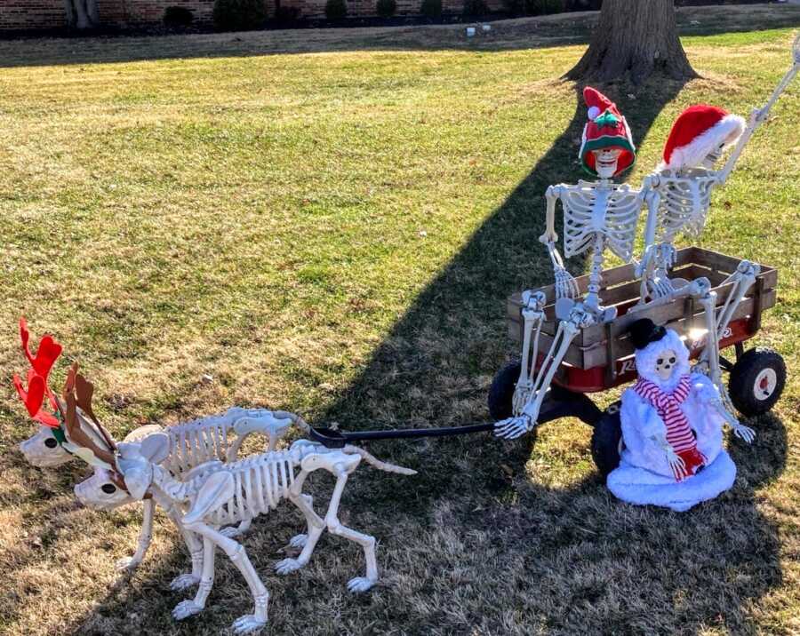 家庭用骷髅装饰创造圣诞庭院场景，两只骷髅被驯鹿拖在马车里