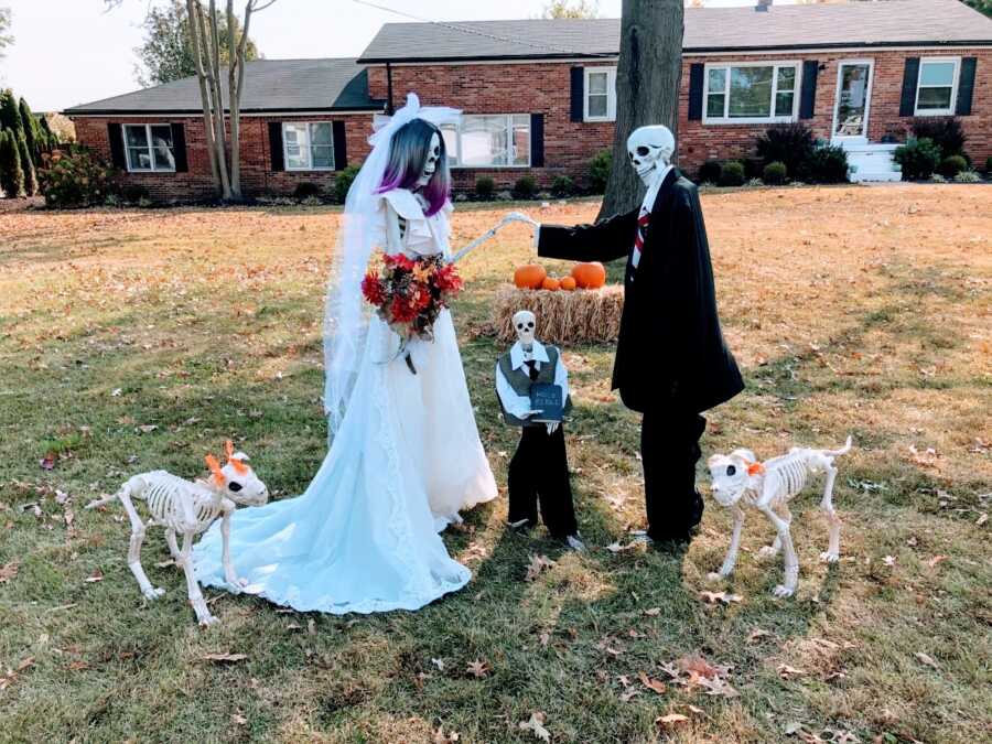 Couple take a photo of their Halloween decorations, two skeletons dressed up as if getting married to one another