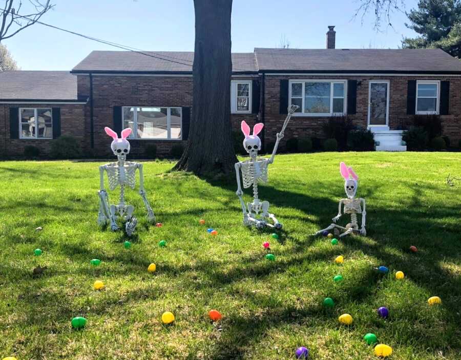 Family decorate for Easter by creating skeleton yard display where the skeletons are doing an Easter egg hunt with bunny ears on