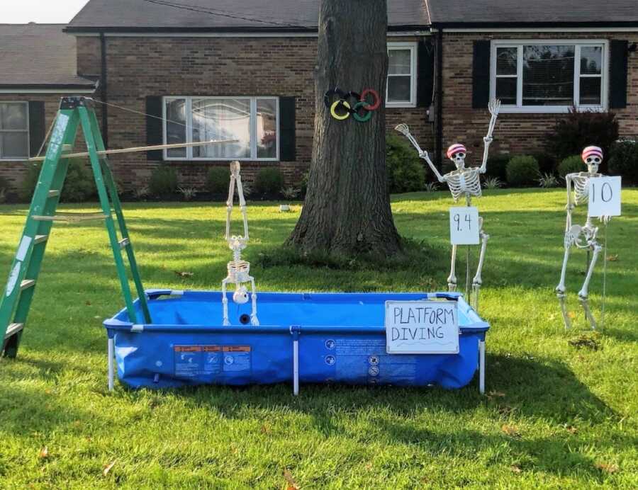 Couple use Halloween skeleton decorations to create a platform diving yard scene for the Summer Olympics