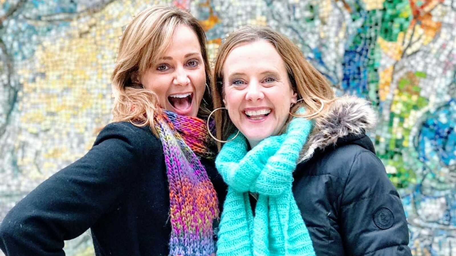 Two mom friends pose for a photo in front of a colorful mural while spending quality time together
