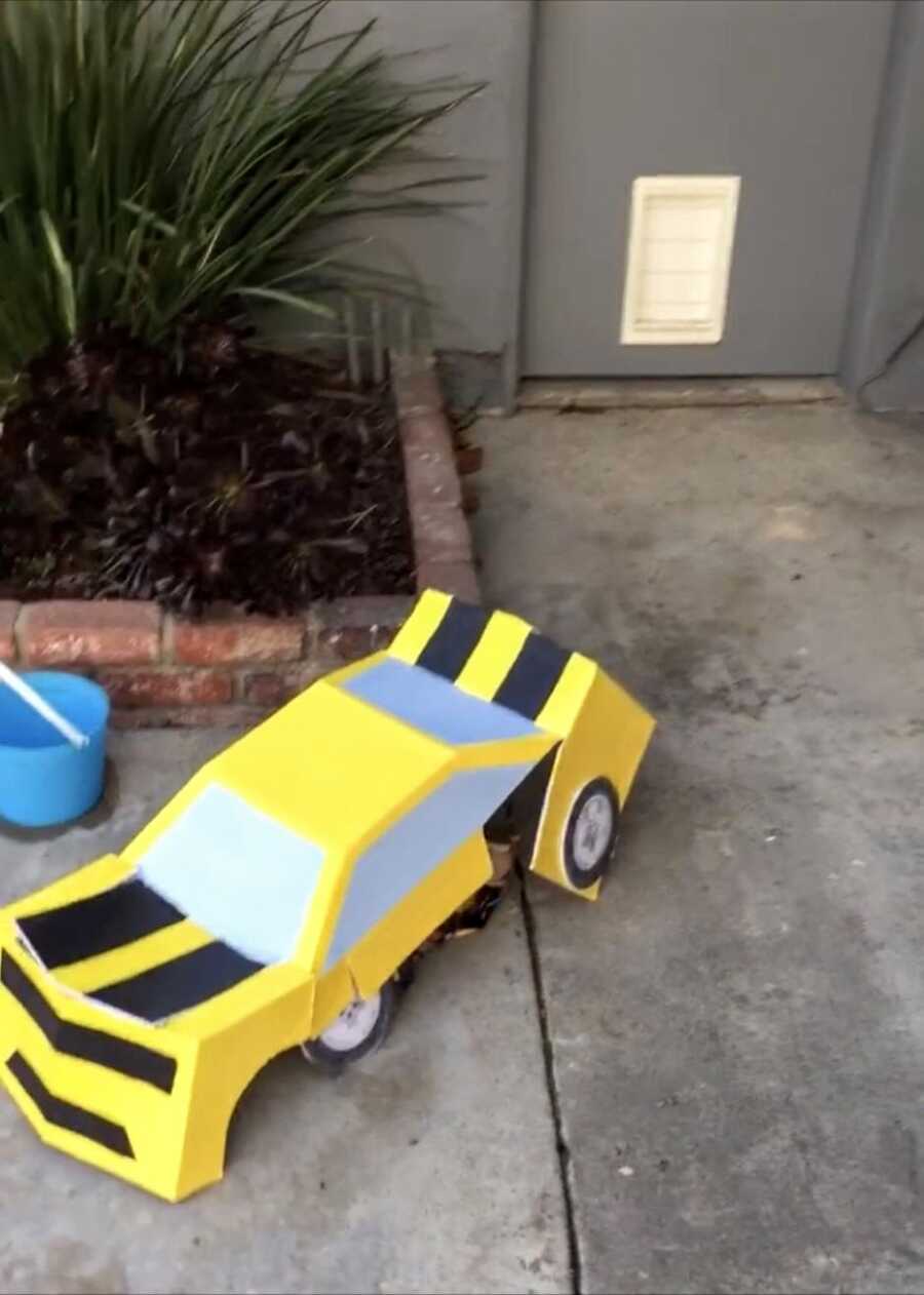 Little boy crouches down on the ground in a homemade Transformers Bumblebee costume, looking like a toy car