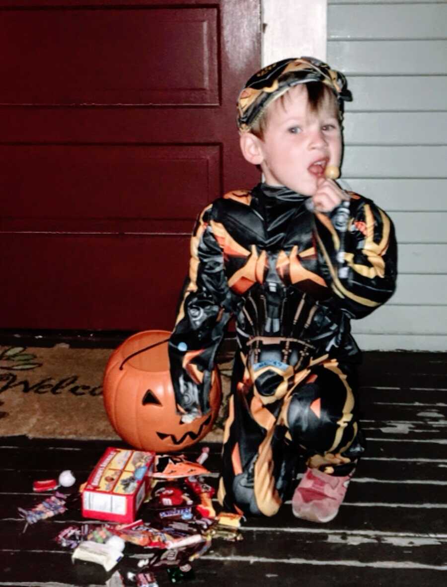 Little boy sits on the front porch after trick or treating in a Bumblebee costume while eating a sucker