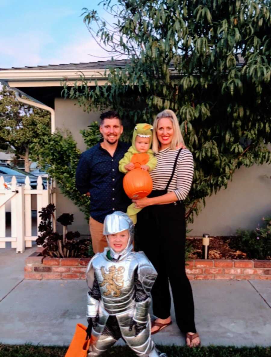 Family of four take a photo together on Halloween, one son dressed as a knight and the other a dinosaur