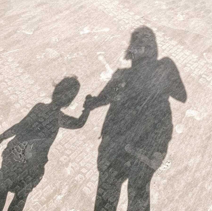 Mom takes a photo of her and her daughter's shadows while they walk together holding hands