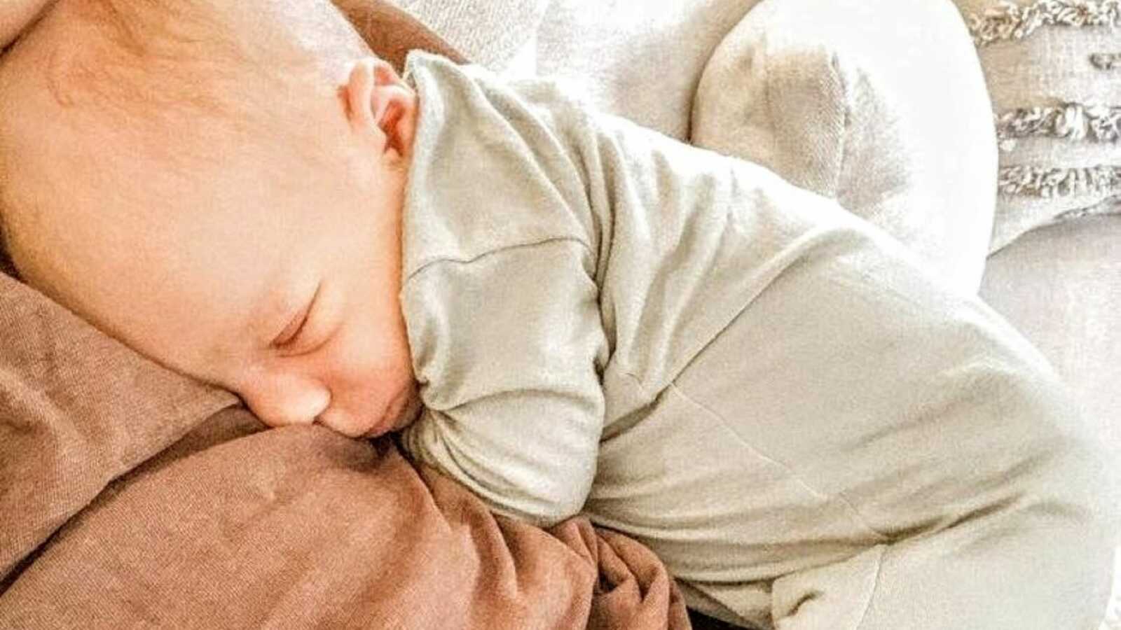 Newborn sleeps peacefully on his mom's chest and belly while wearing a neutral-colored onesie