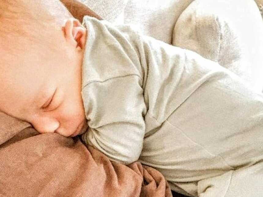 新生儿穿着中性色的连体衣，睡在妈妈的胸部和腹部