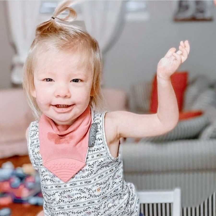 Little girl with hypotonia and Coffin-Siris Syndrome smiles during playtime in a tank top with a pink bib