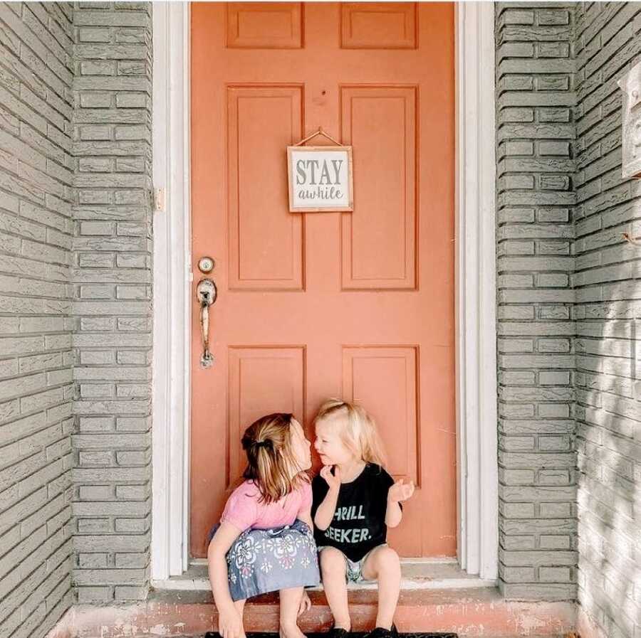 Two sisters pose in front of a their family home's front door while going in to share a kiss