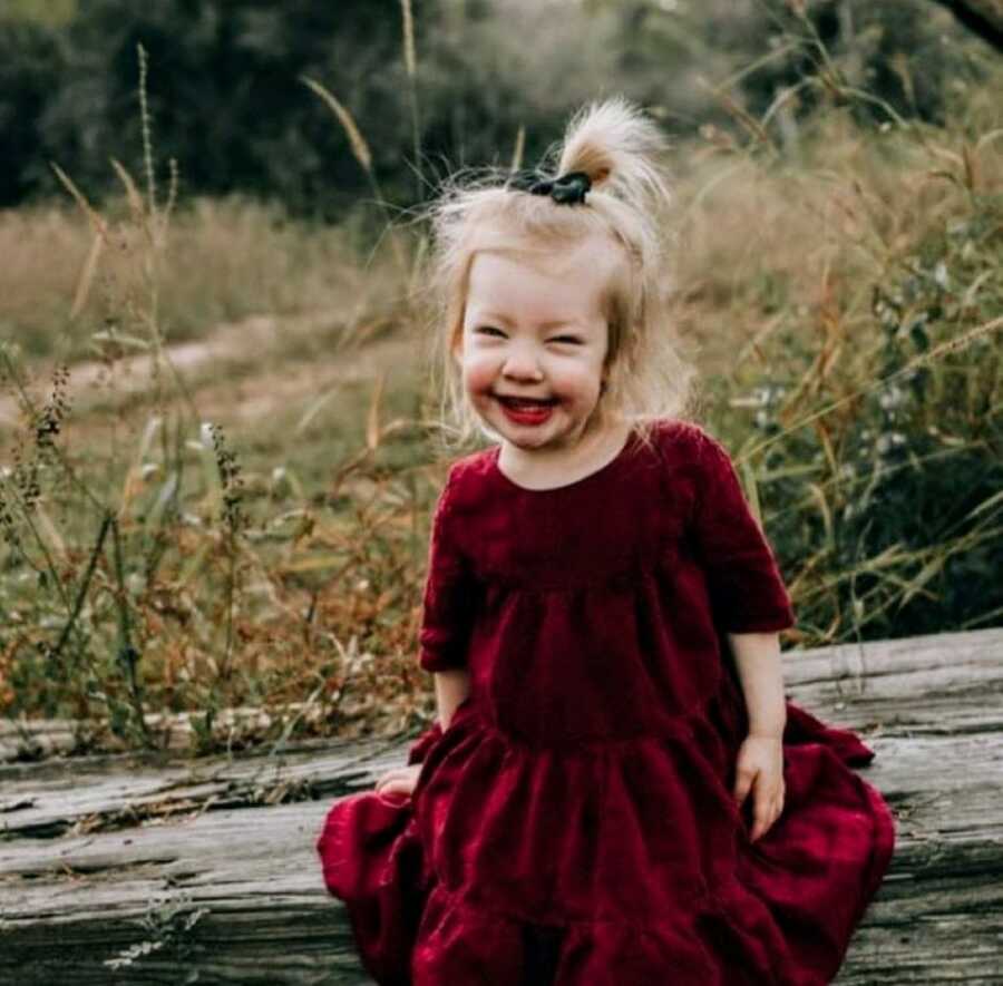 Little girl with Coffin-Siris Syndrome smiles big while wearing a velvet red dress for a Christmas photoshoot