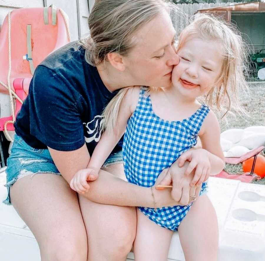 Mom kisses her daughter with Coffin-Siris Syndrome on the cheek while enjoying a pool day in the summer