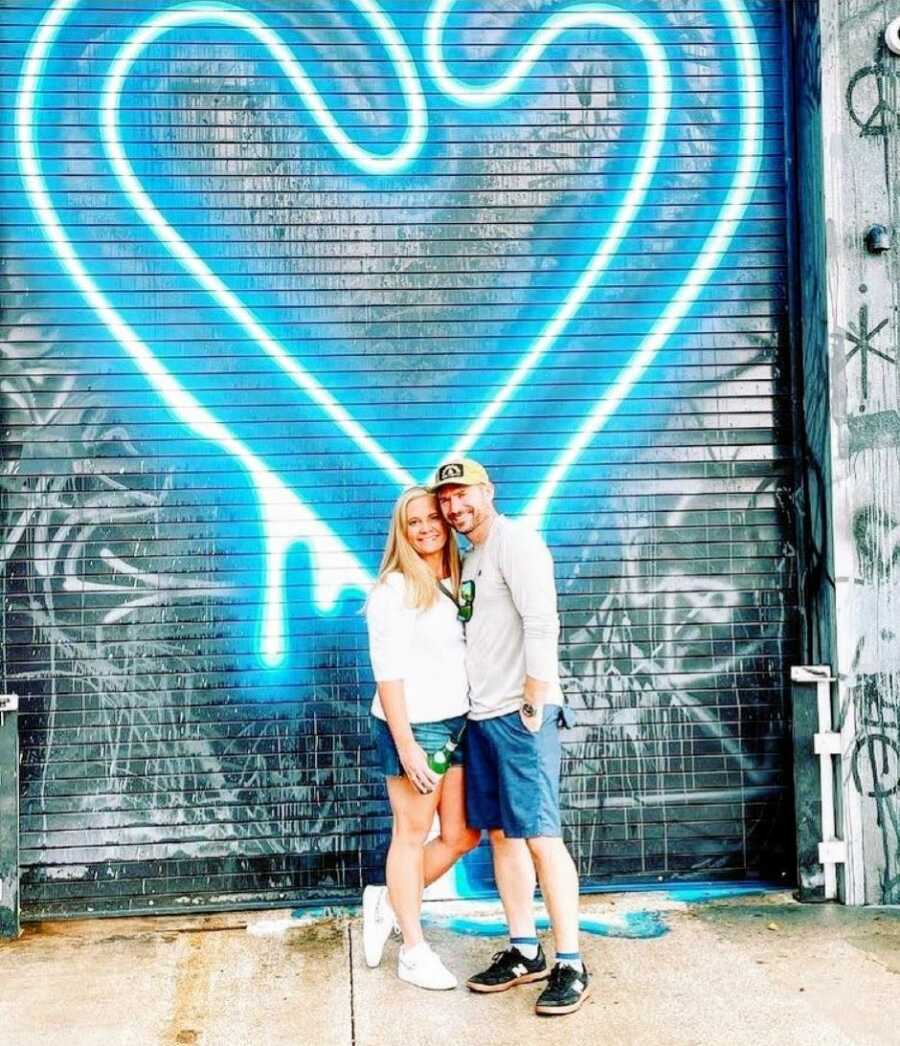 Husband and wife take a photo in front of a giant graffiti blue neon heart