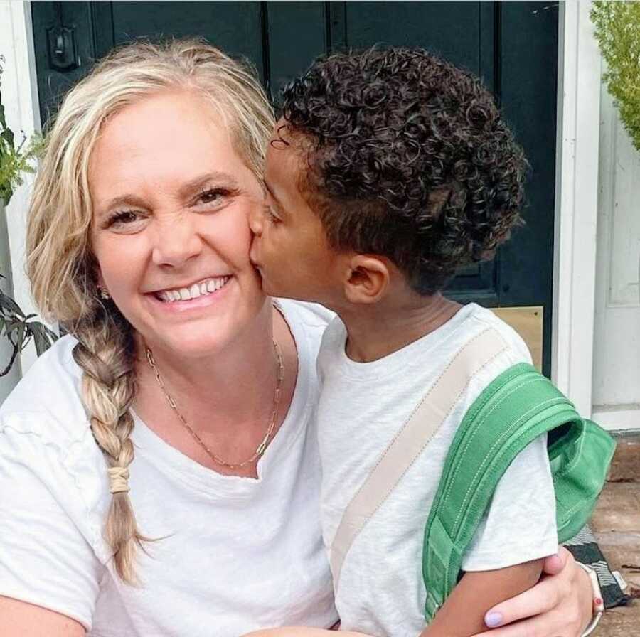 Mom of seven smiles big while her youngest adopted son kisses her on the cheek for a photo before school