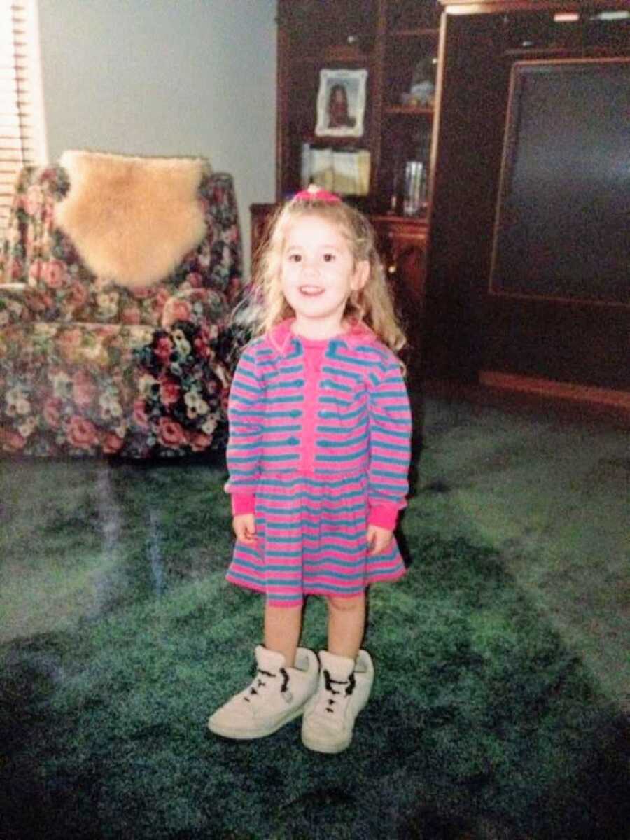 Little girl with OCD stands in her dad's tennis shoes while wearing a pink and blue-striped dress