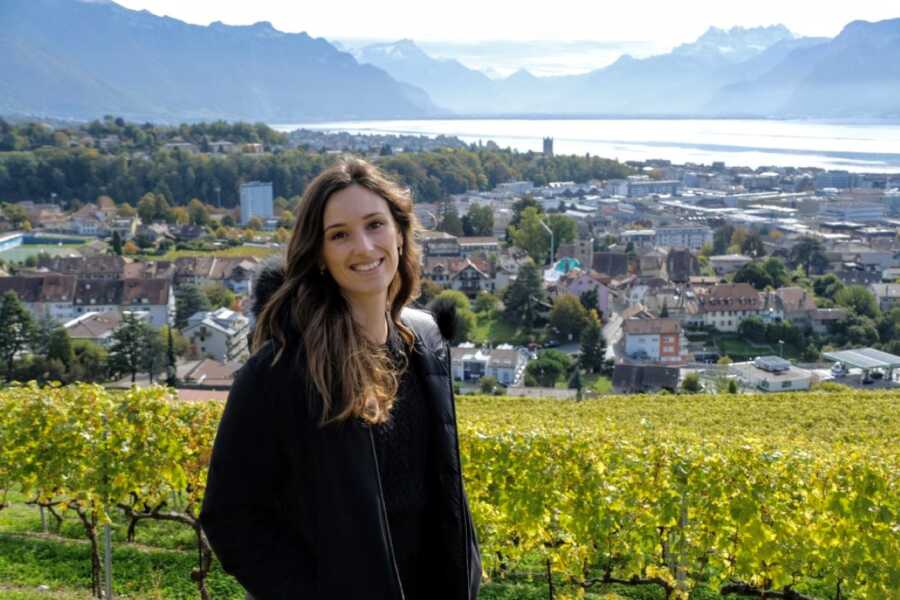 Woman smiles for a photo while on a hike, the background overlooking a city in Switzerland