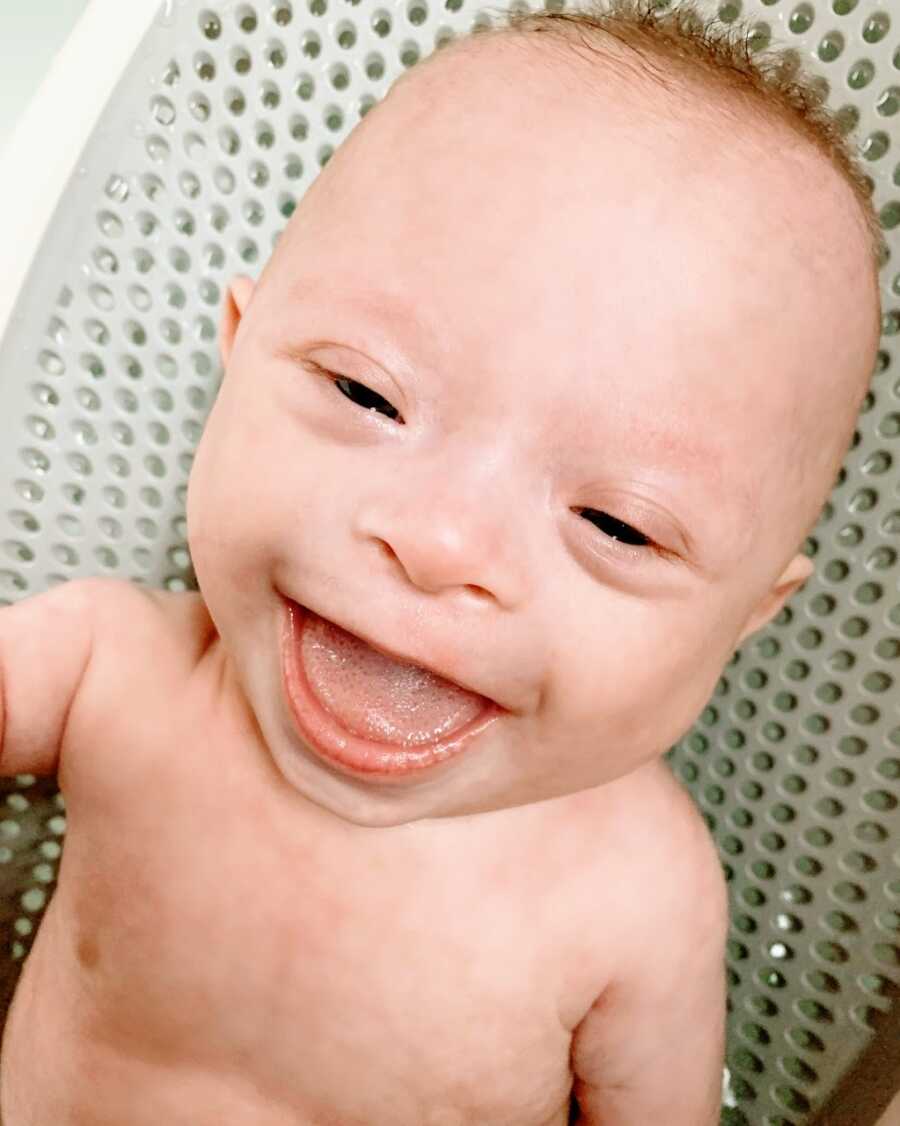 Young baby boy with Down Syndrome smiles big during bath time