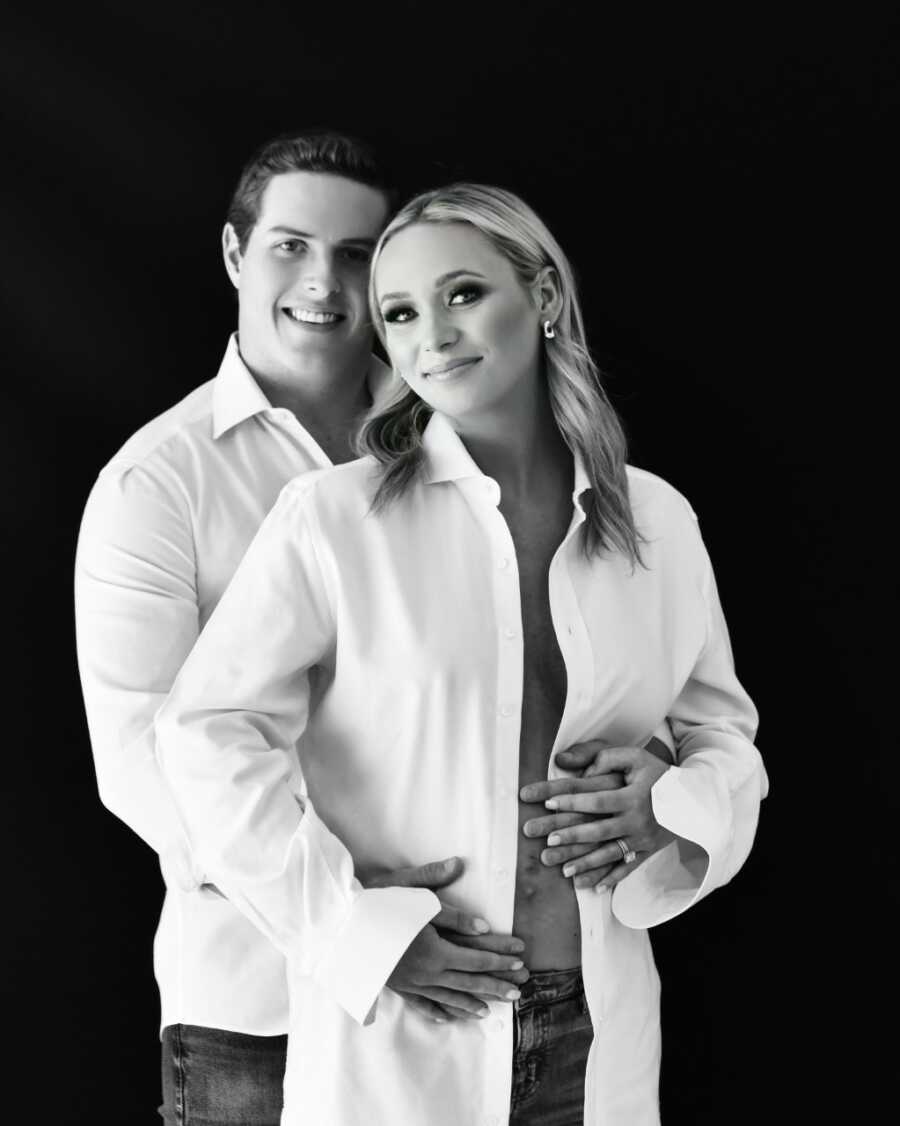 Married couple take black and white maternity photos together in matching white button down shirts