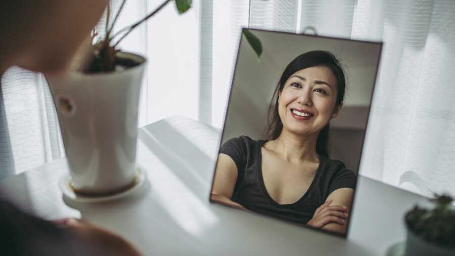 Woman confidently smiles at a reflection of herself in the mirror. 