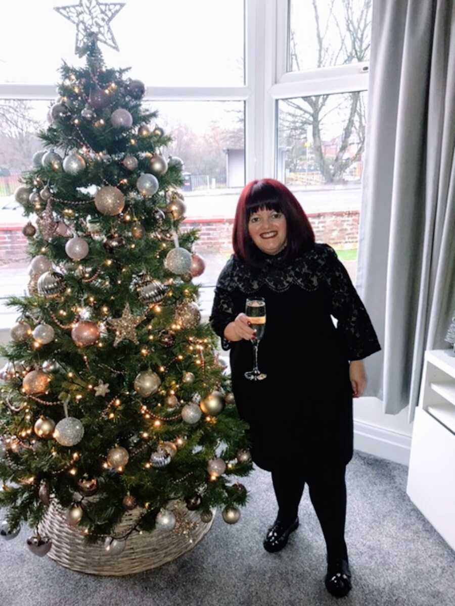 A woman with RSS stands next to a Christmas tree