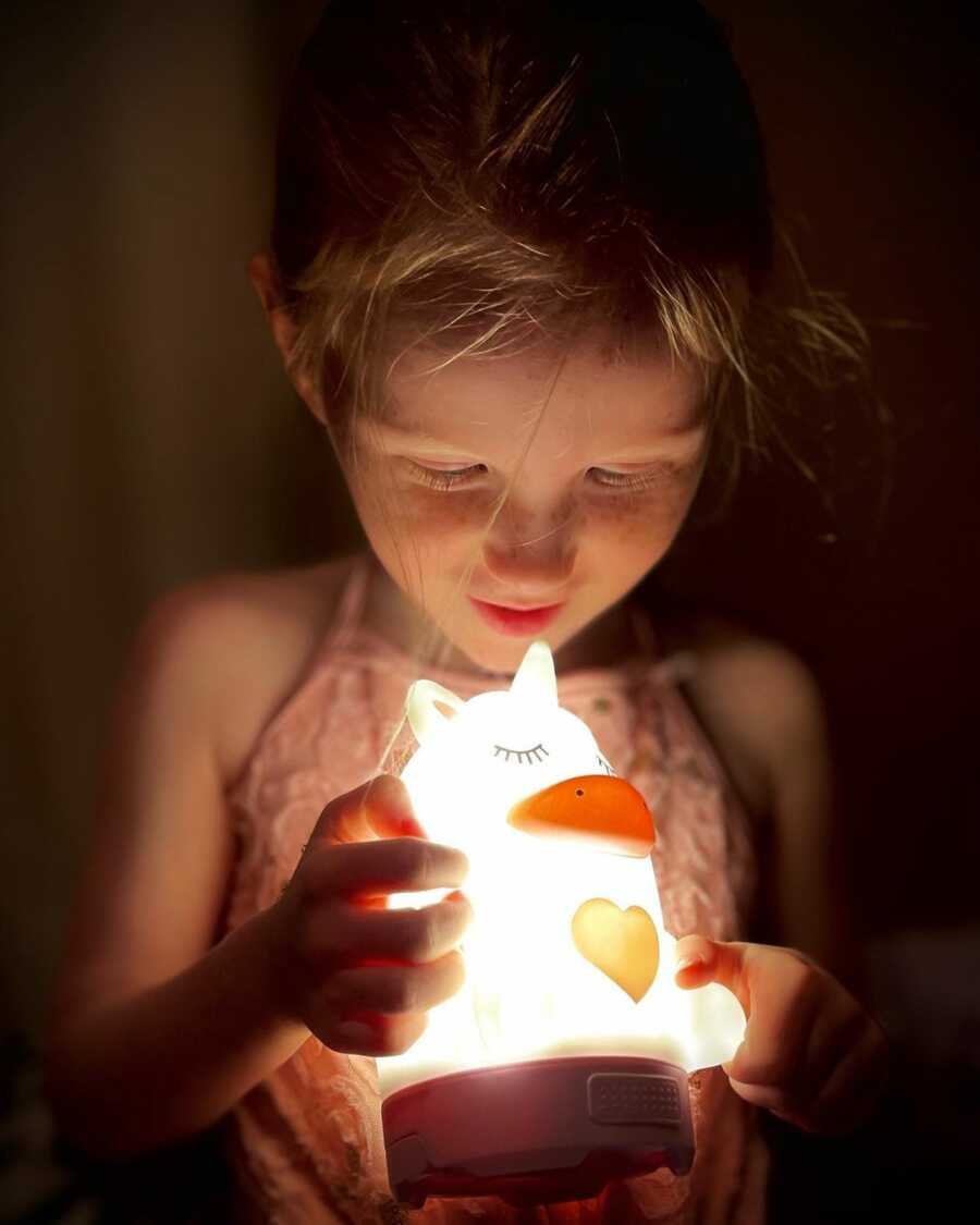 A young girl stares in wonder at a glowing night light animal. 