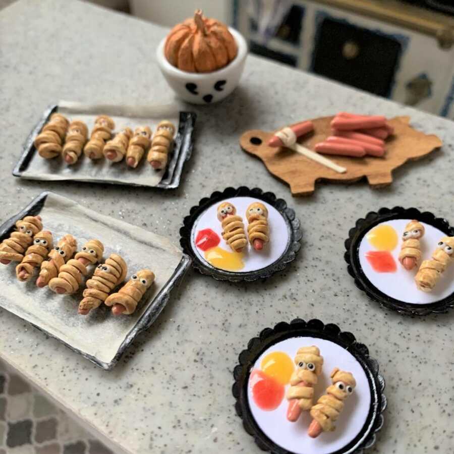 Miniature Halloween mummy hot dogs made from sculpted clay.