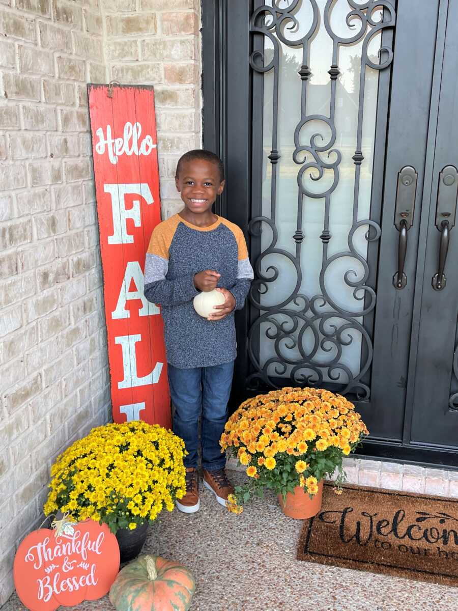 Dwayne stands by the front door, holding a small white pumpkin. 