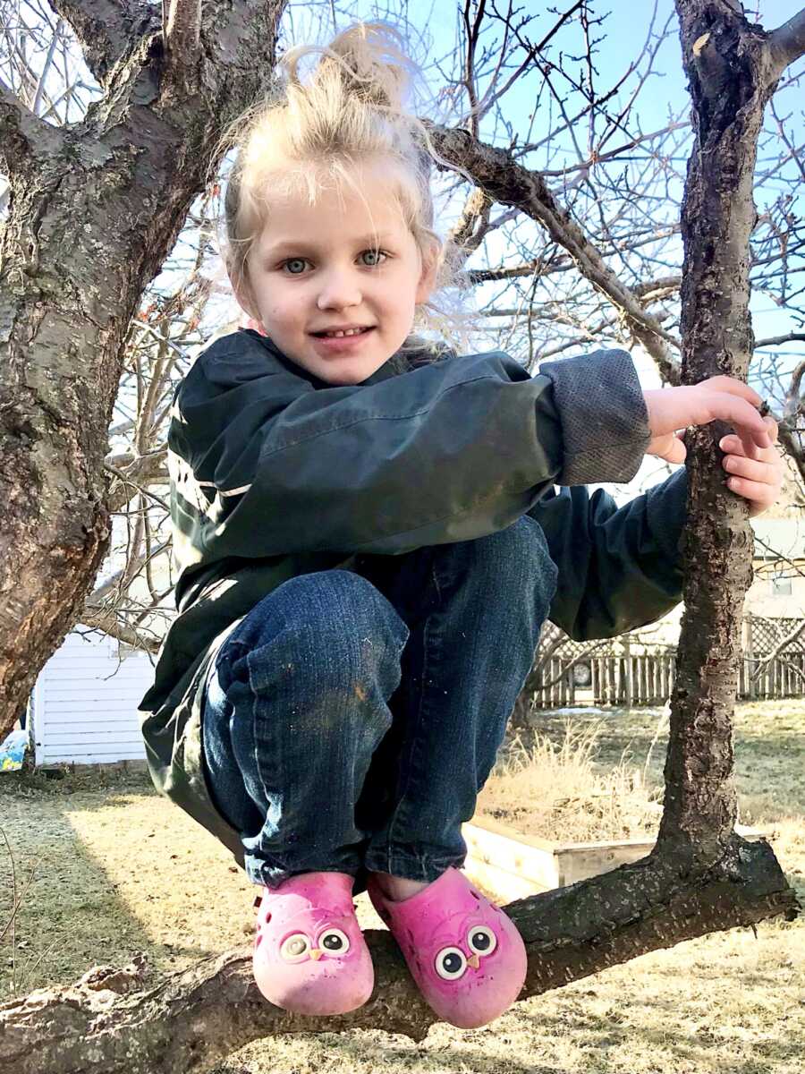 Evie, wearing pink owl crocs, perches in a tree she climbed.