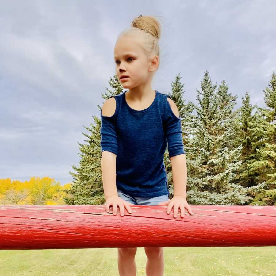 Evie climbs on a red fence post in a field of trees. 