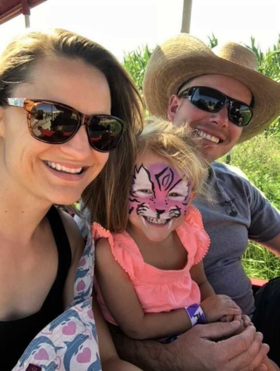 Mom and dad embracing daughter with face paint