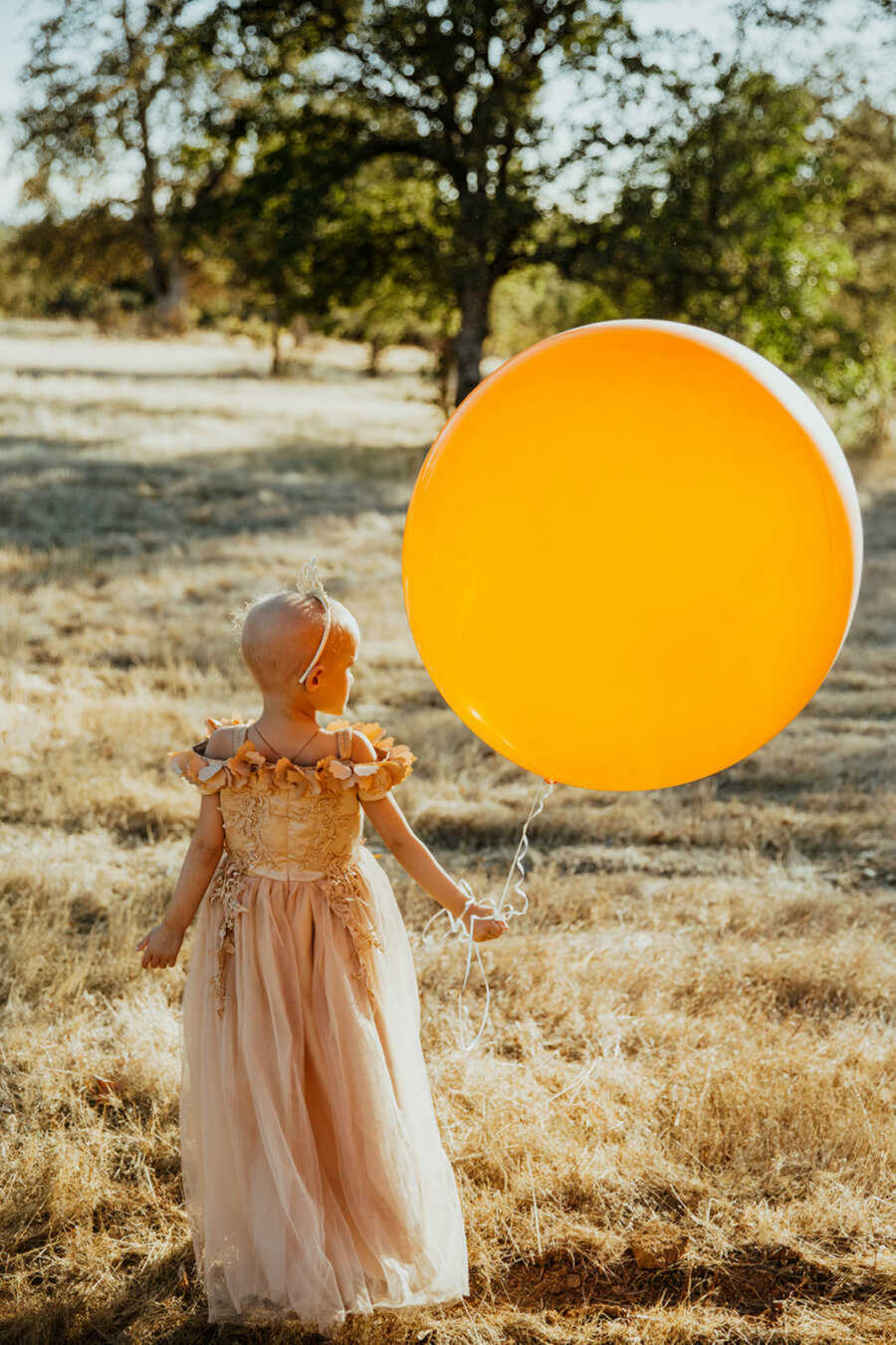 Girl with leukemia holding large yellow balloon in sunshine