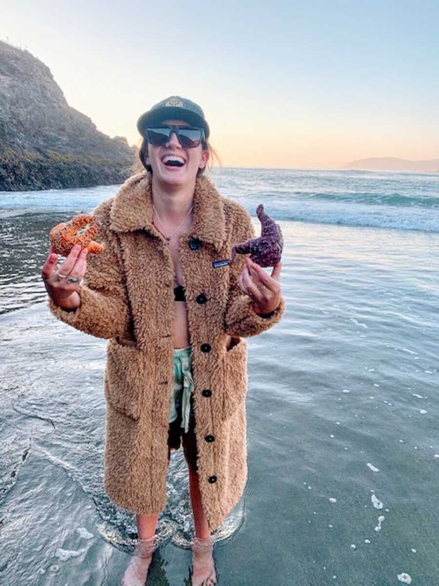Woman holds up starfish while standing in water