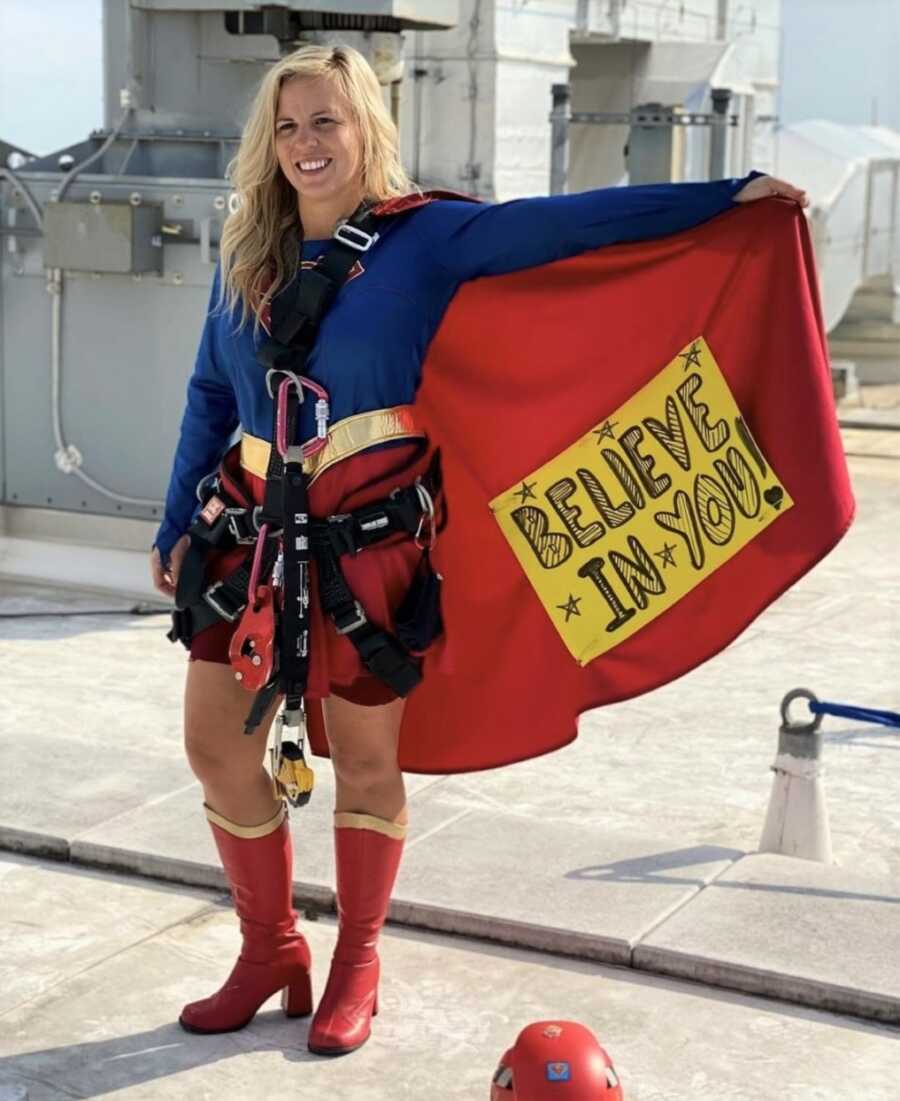Loren wears a Supergirl costume with a sign that says "Believe in you!"