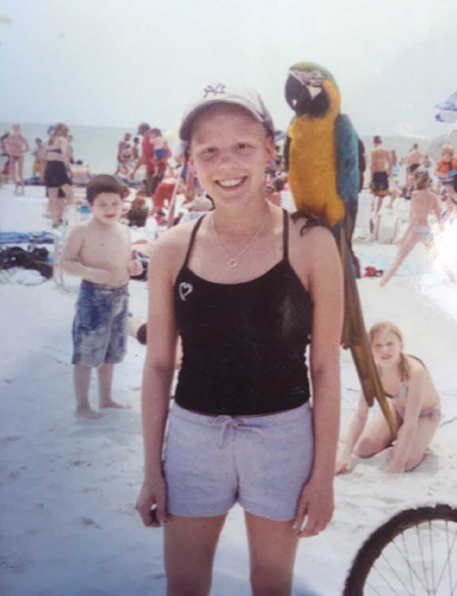 Young Loren Jewell poses at the beach with a macaw on her shoulder.