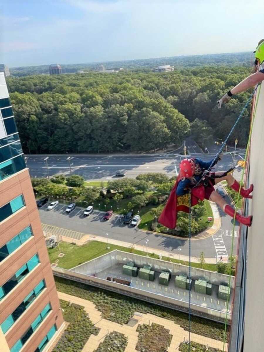 Loren repels down the side of the children's hospital in her Supergirl costume.