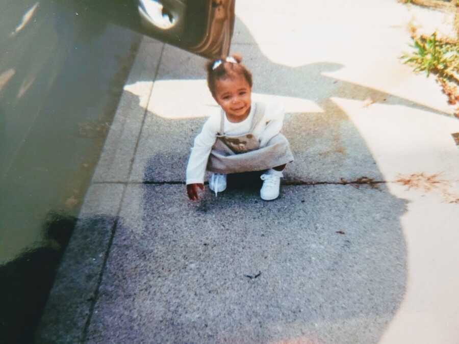 young girl wearing grey dress playing on sidewalk