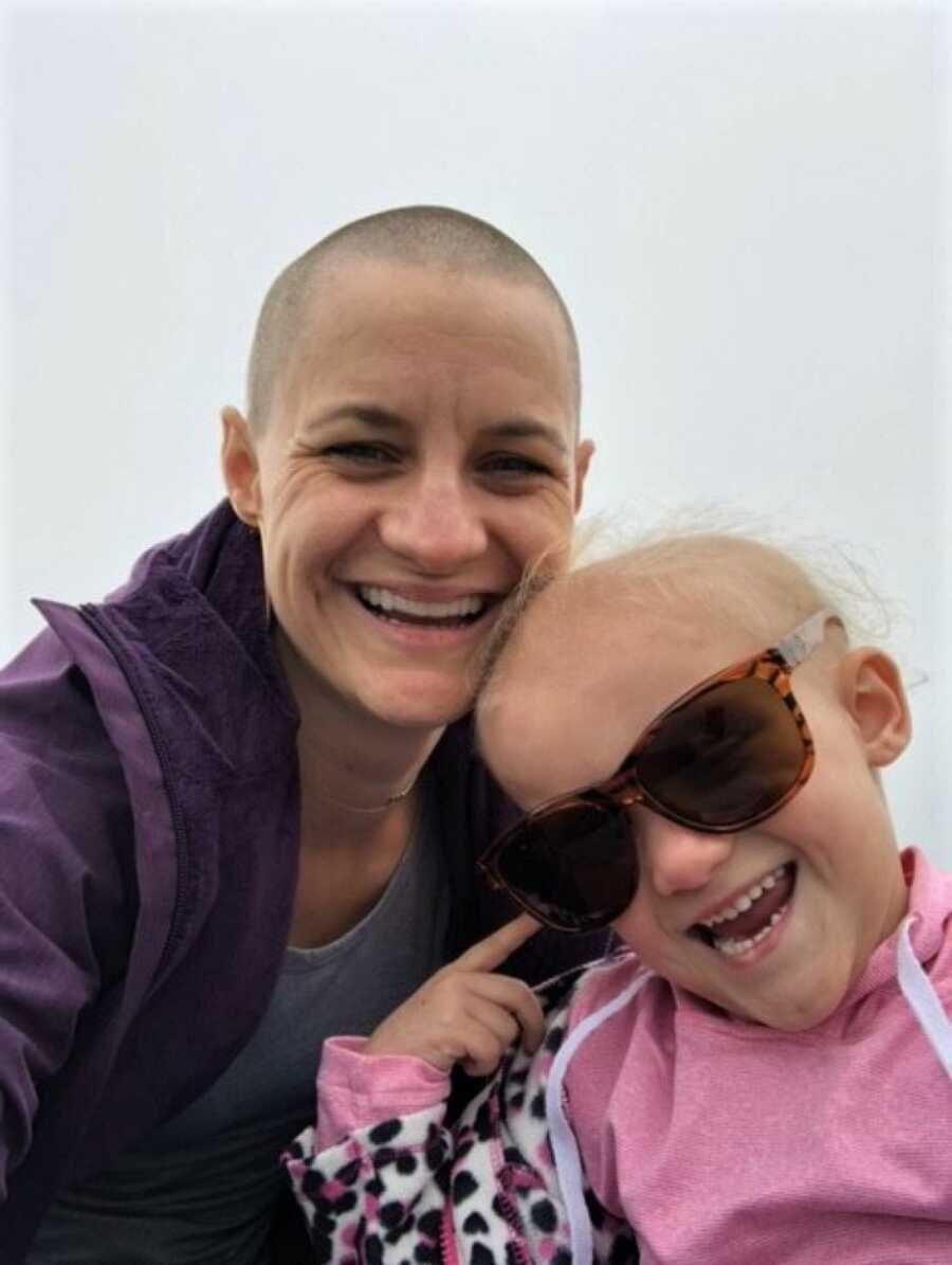 Bald mother and daughter smiling into camera