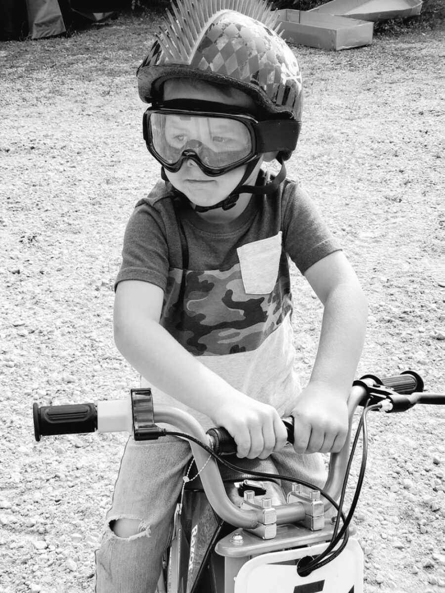 一张黑白照片中，孩子骑着自行车，戴着护目镜和头盔