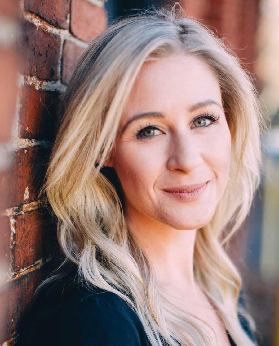 Blonde woman smiling resting on a brick wall