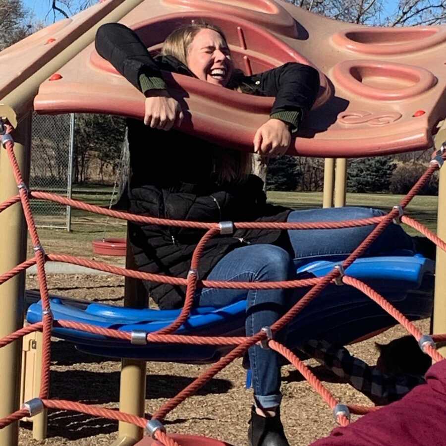 woman laughing as she is stuck in the jungle gym