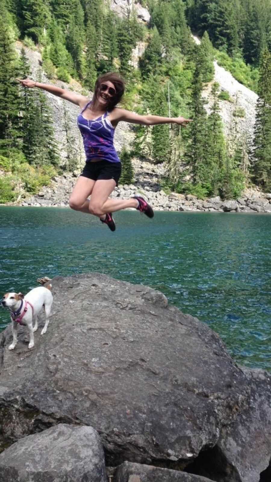 一个女人带着一只白色的狗出去远足，在岩石上跳跃