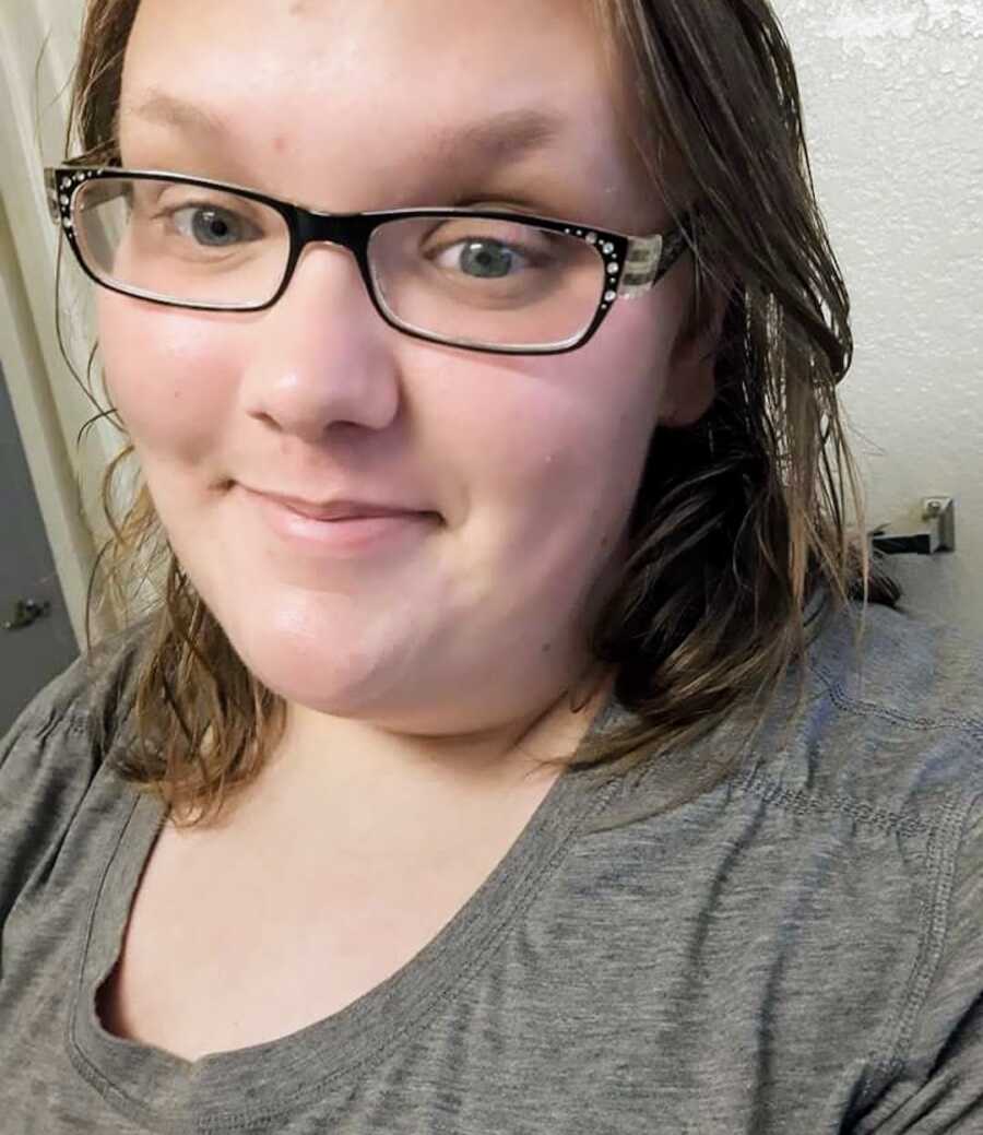 Woman who survived abuse wearing a grey shirt and glasses