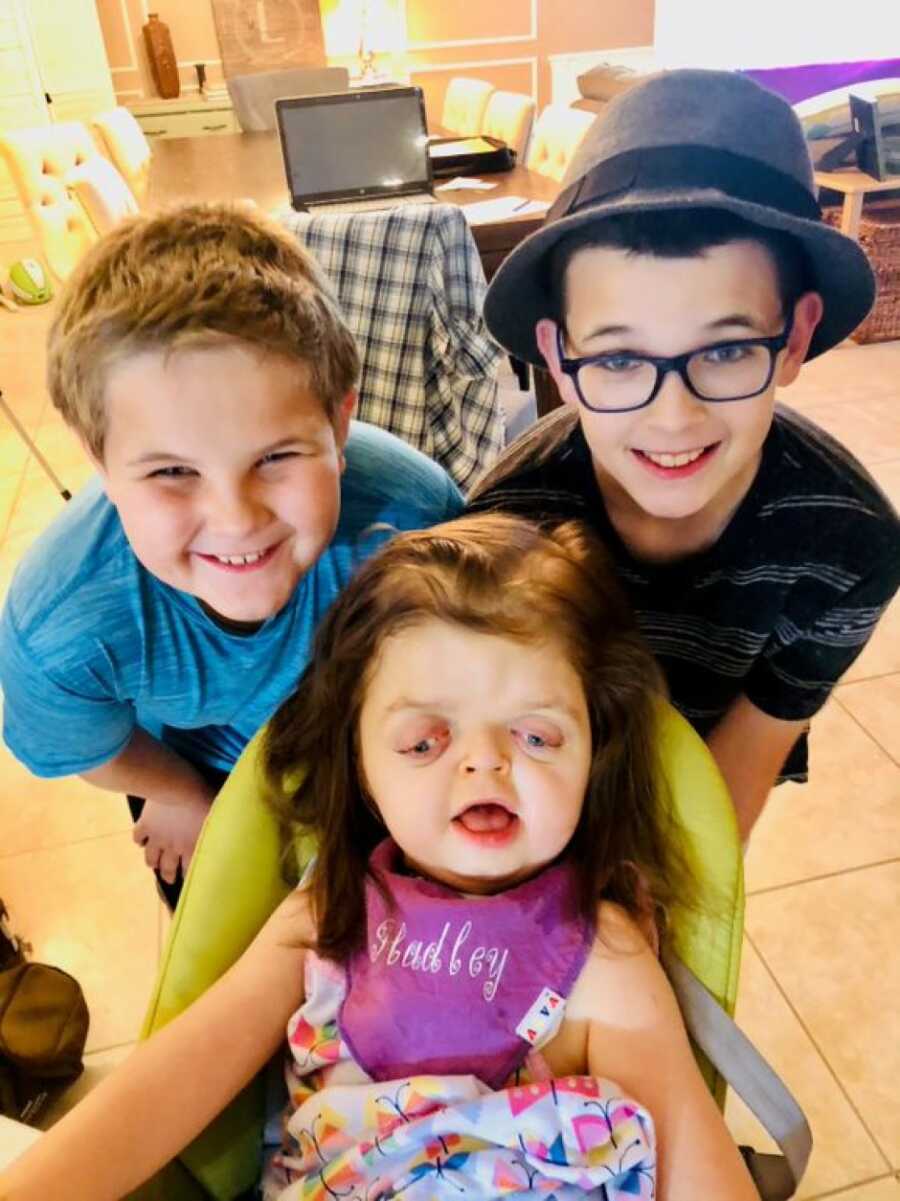 older brothers posing for a picture with their younger sister while she is sitting in a green chair