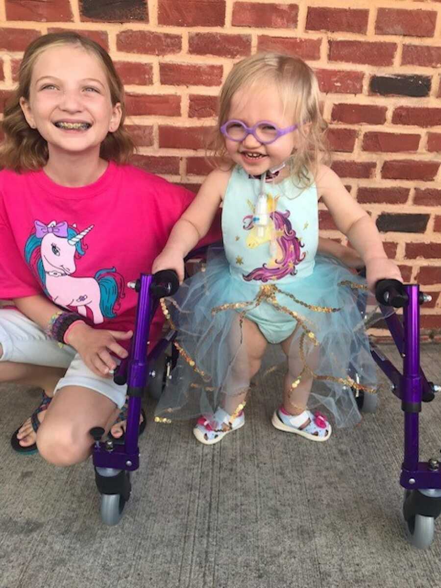 baby girl using a purple walker to stand by her sister