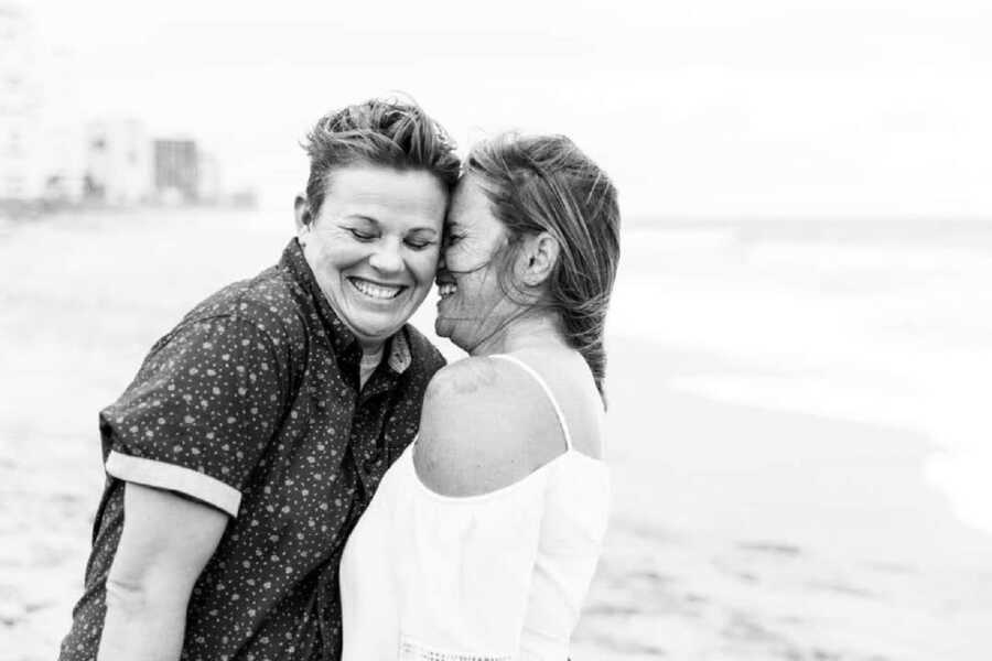 LGBT couple smile and hug in front of the ocean