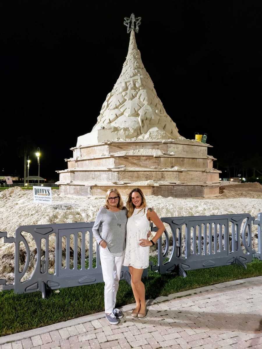 two women posing in front of a Christmas tree sculpture 