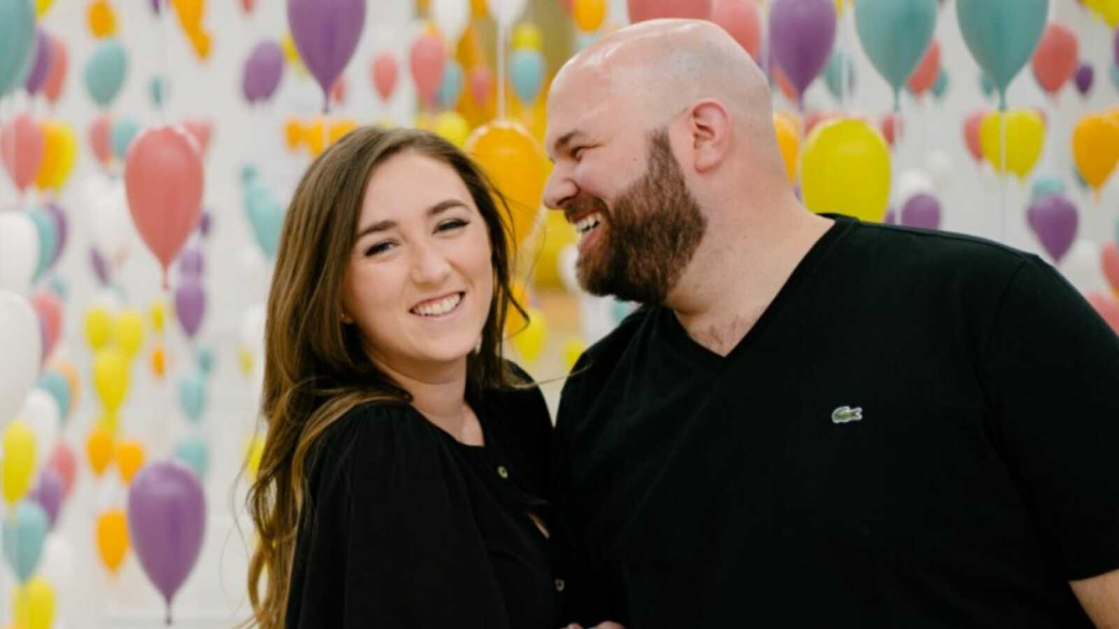 couple dressed in black posing in front of green, yellow, pink, and purple balloons